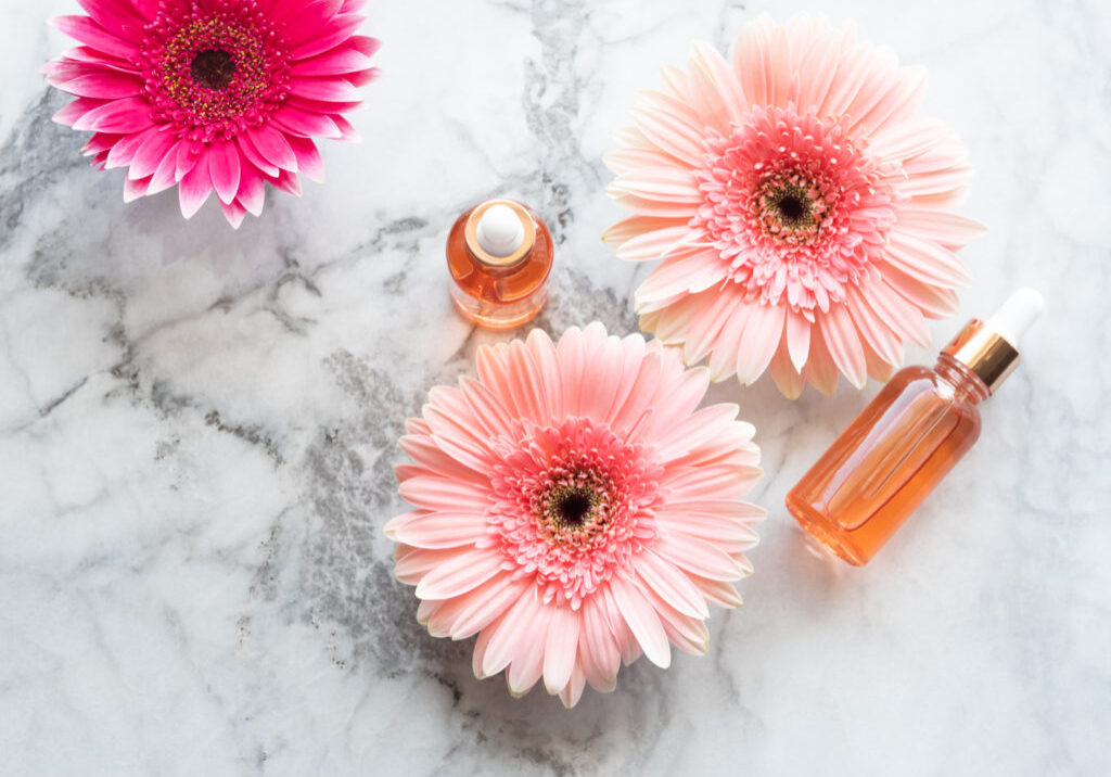 Pink flowers and beauty serum in dropper bottles on marble table. Skin care concept with flowers and herbs. Natural cosmetics