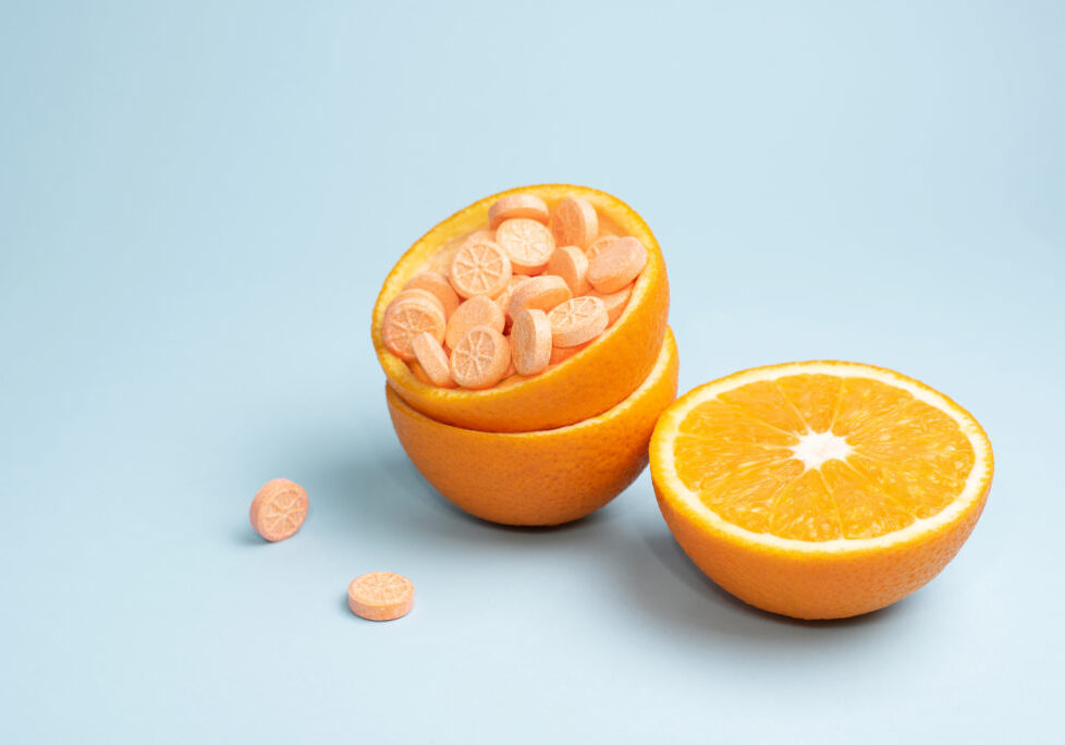 Half orange and peel with vitamin C tablets on a blue background, close up. Vitamin C pills as an alternative to citrus fruits. Immune booster concept.
