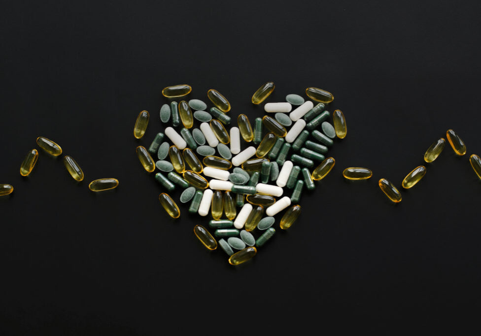 Health support concept. Omega 3, spirulina, chlorophyll, magnesium capsules in heart shape on black dark background. Dietary supplements. Heart made of pills. Flat lay